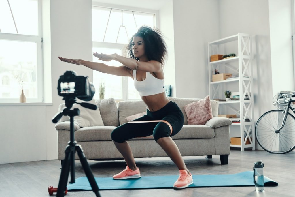 Beautiful young African woman crouching using strap while making social media video By gstockstudio