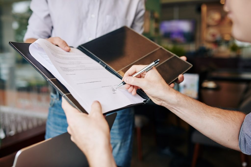 Close-up image of businessman signing contract in hands of his business partner By DragonImages