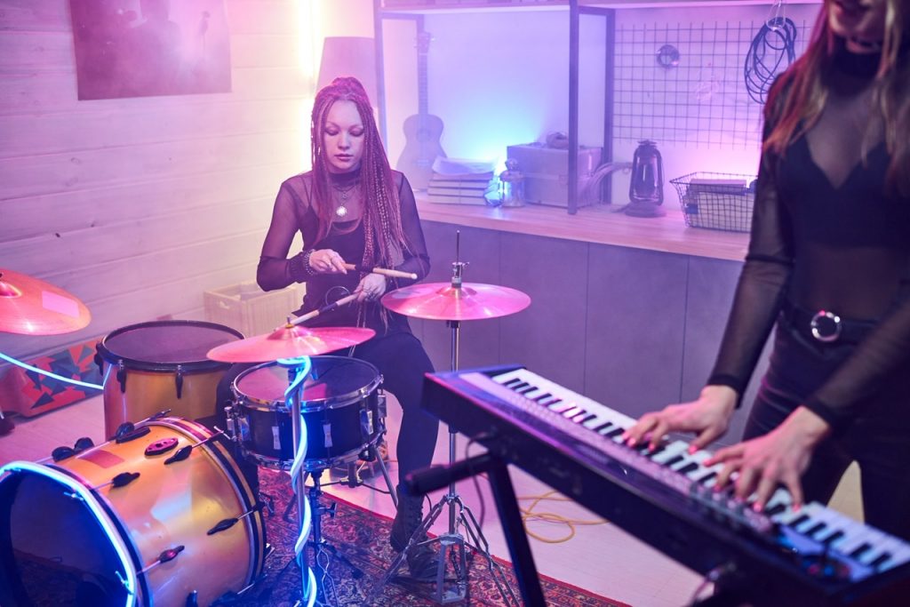 Two young women playing on musical instruments during rehearsal in the music studio By Pressmaster