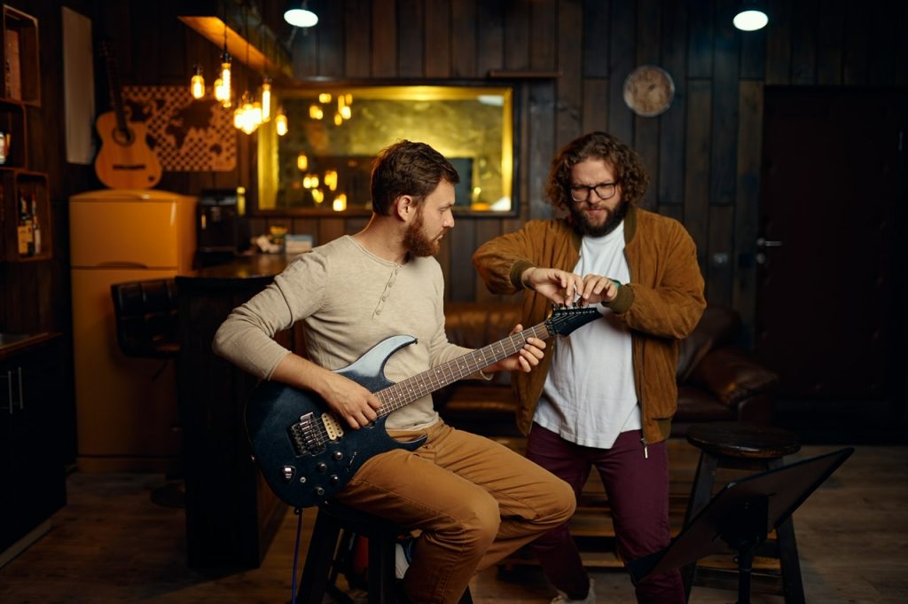 Guitar training music lesson at professional studio. Musician teaching young guy to tune instrument By NomadSoul1