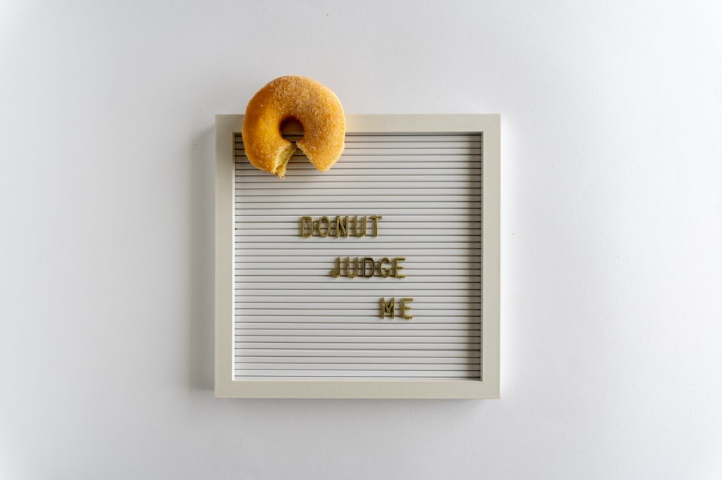 Letterboard With Words That Spell Donut Judge Me ,with a fresh donut, in golden letters, on a white background, horizontal By lizzykomen