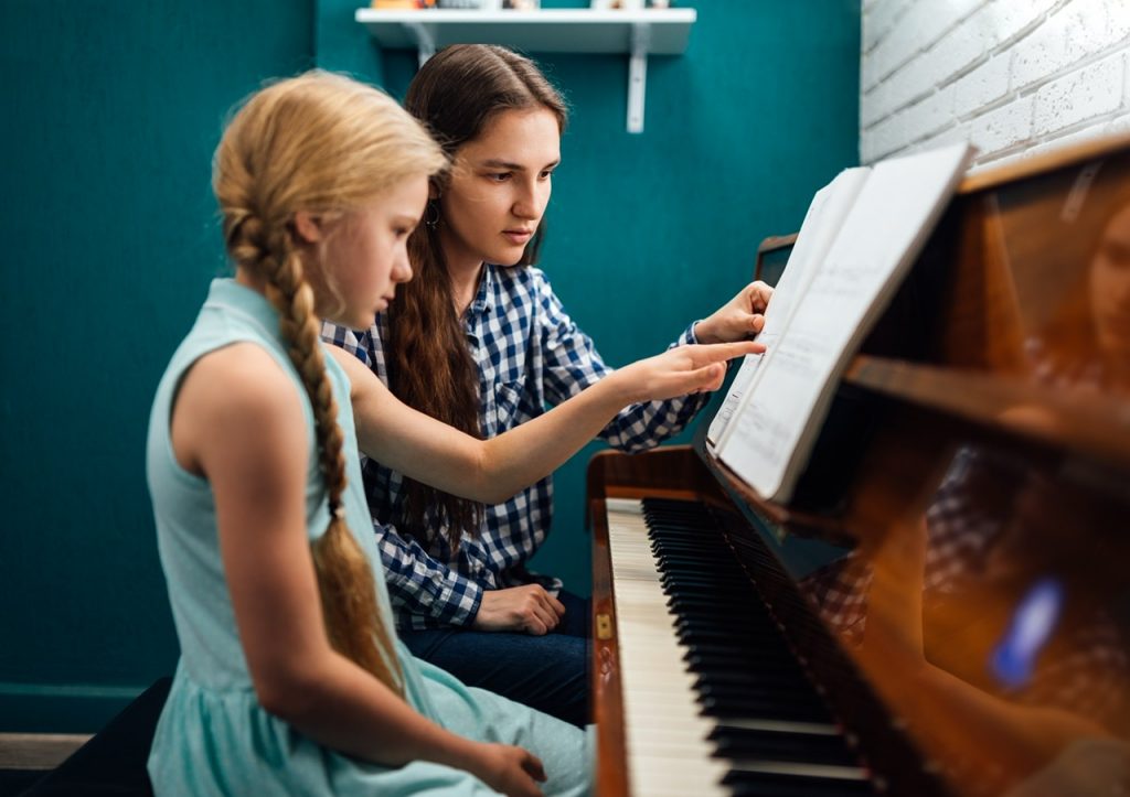 Piano teacher giving a music lesson to her student, explaining notes, home studying By Artranq