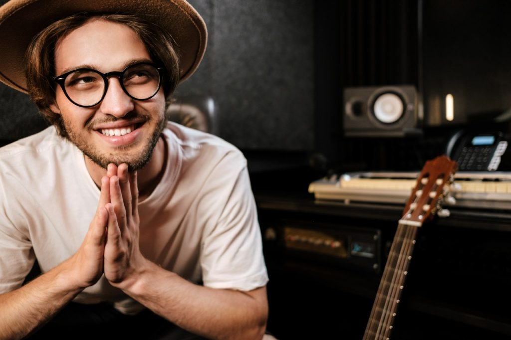Portrait of attractive smiling singer man happily creating music in sound recording studio. Music production By garetsworkshop