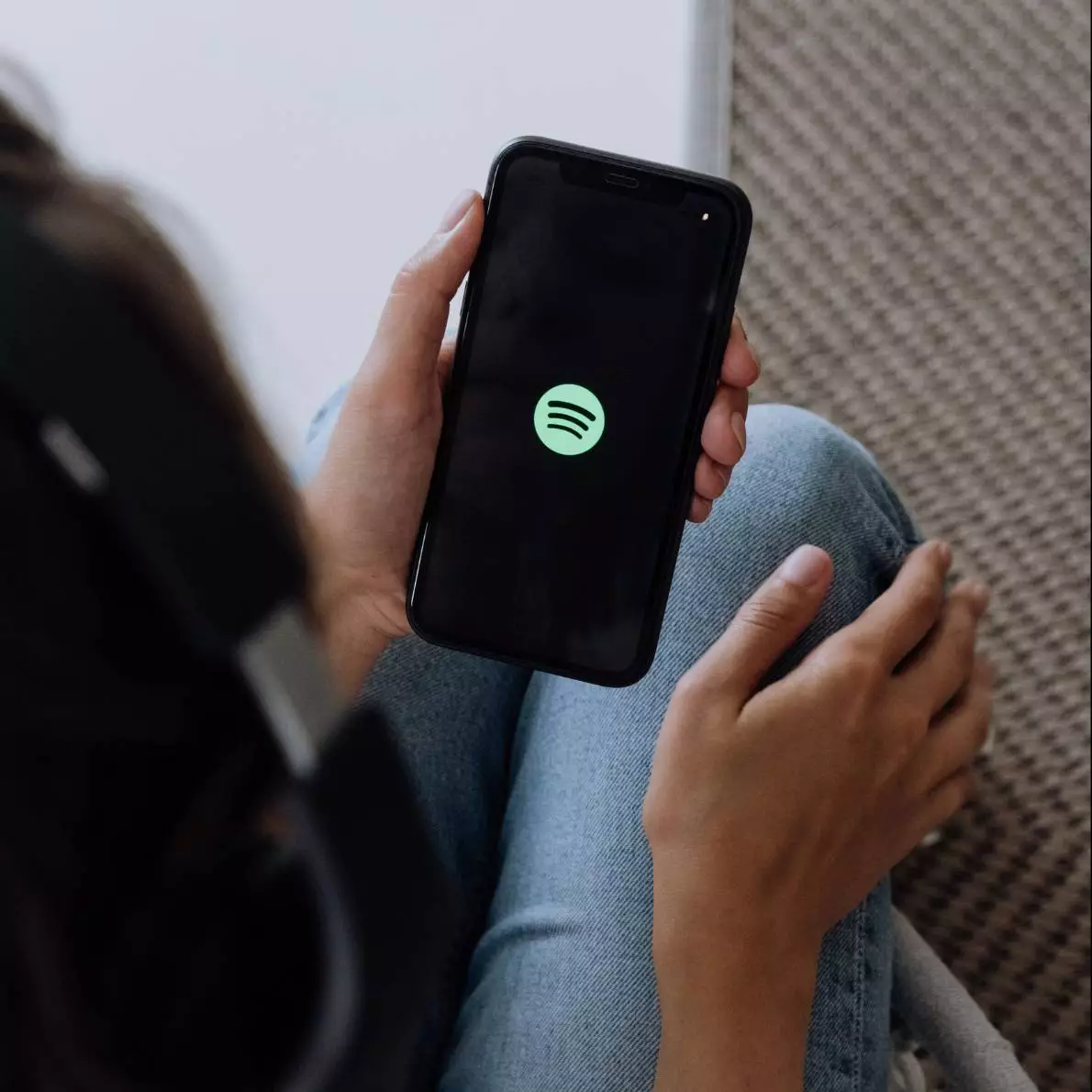 Spotify app open on phone. Person holding phone with headphones on.