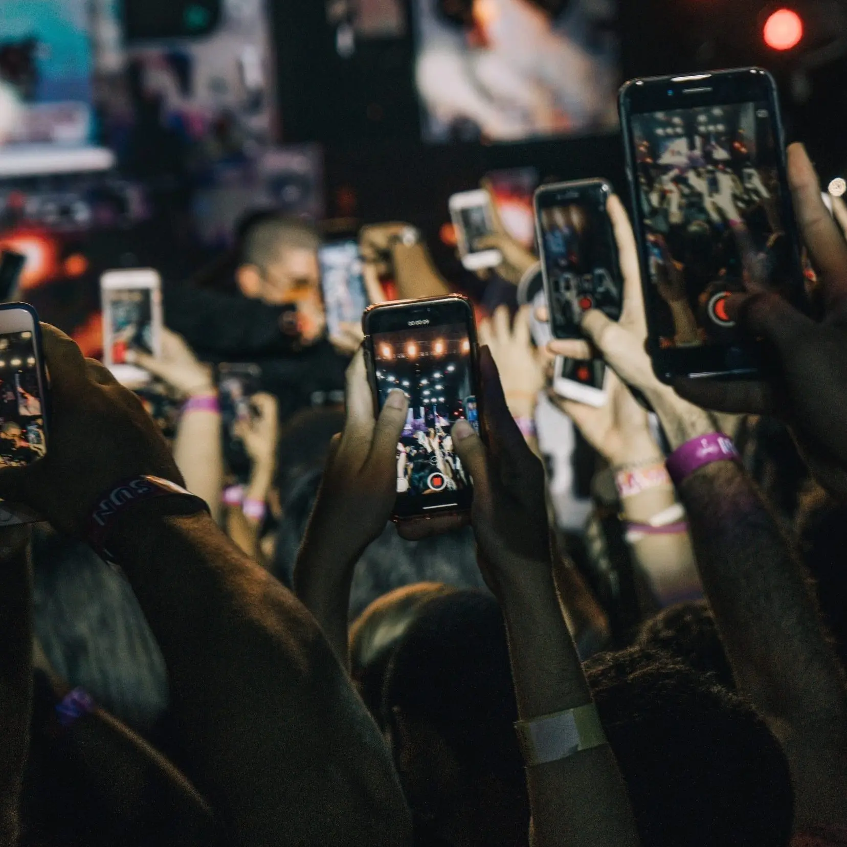 Crowd of people holding up their phones recording a live music show moment to put online.