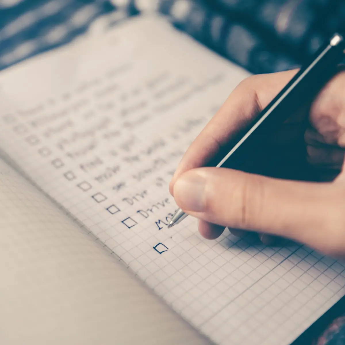 Person's hand writing a music release checklist on lined paper with a black pen