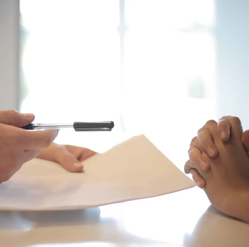 A manager holding a pen and paper out to an artist for them to sign.