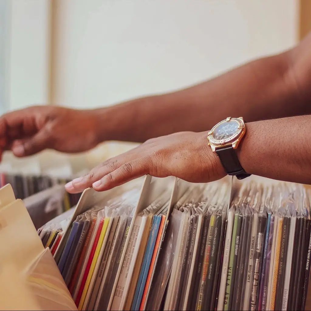 tan male hands with a wristwatch searching through vinyl that has been distributed in a shop