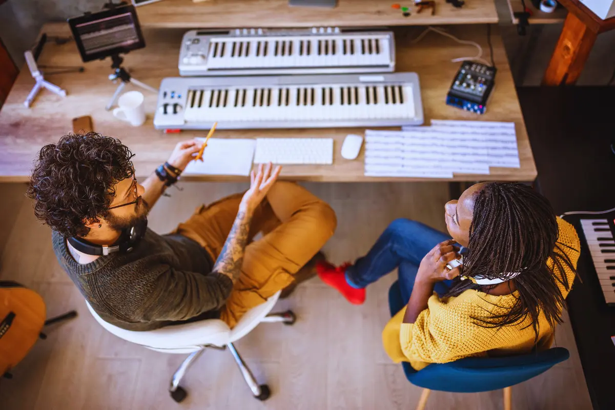 find music collaborators as two musicians discuss ideas in a creative studio with keyboards and sheet music.