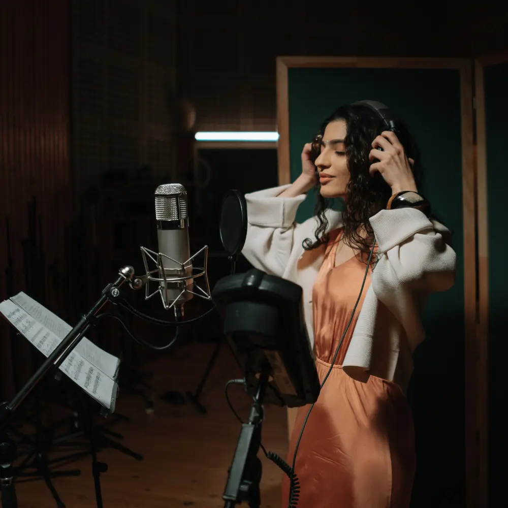 A female vocalist wearing headphones records in a professional studio, highlighting sync agencies for artists