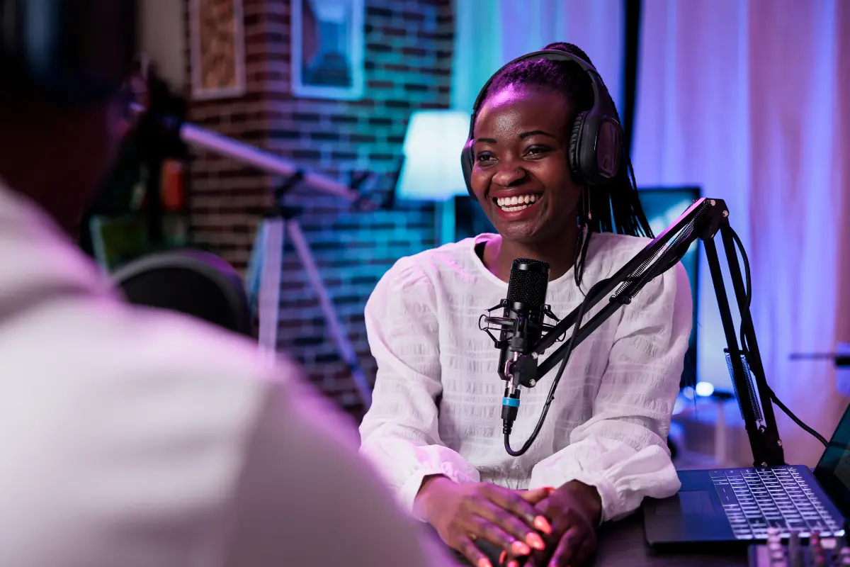 Social media for musicians with a smiling podcaster wearing headphones and speaking into a microphone in a cozy studio
