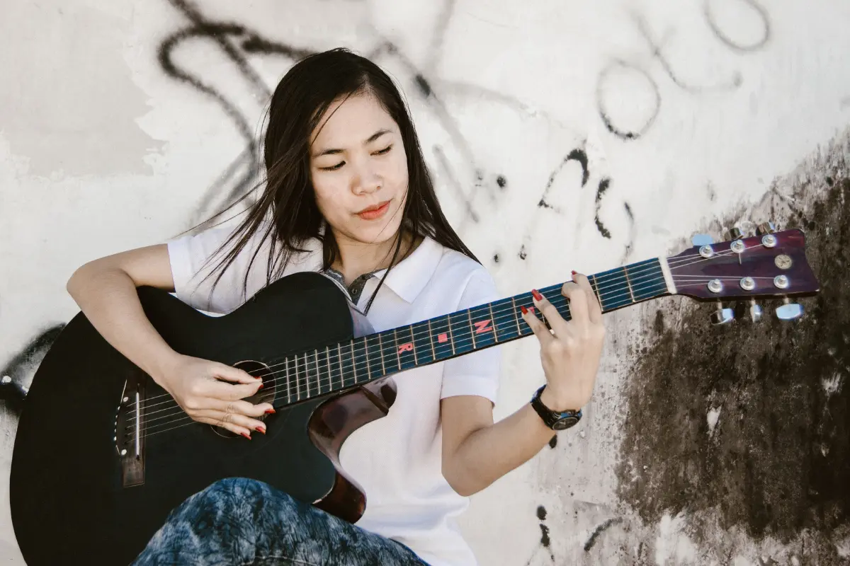 Storytelling for musicians through emotional solo guitar performance by a young woman against a graffiti wall.