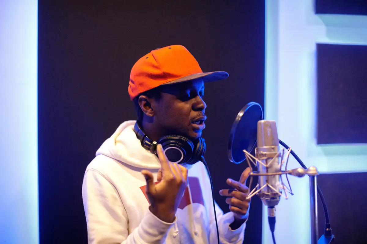 Successful music promotion with a rapper recording vocals in a professional studio wearing a hoodie and red cap