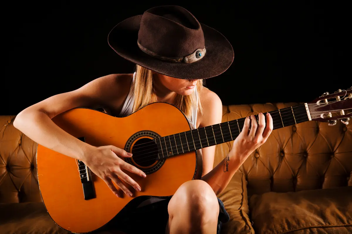 Viral music strategies shown by a woman in a cowboy hat passionately strumming an acoustic guitar on a vintage couch.