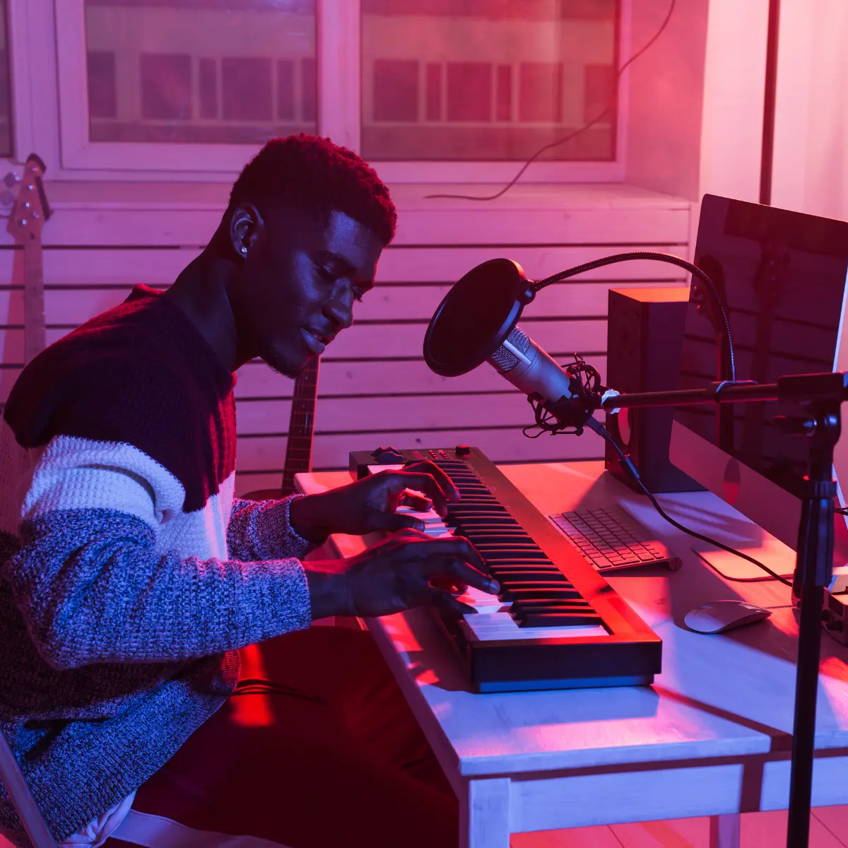 Music producer playing a MIDI keyboard near a microphone in a colorful home recording studio.