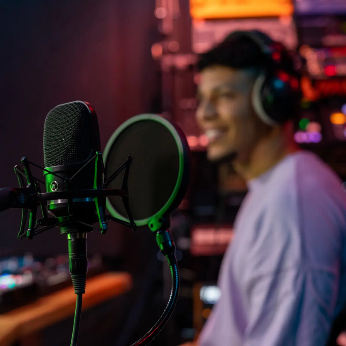Music producer recording vocals with studio microphone and headphones in a colorful sound booth.