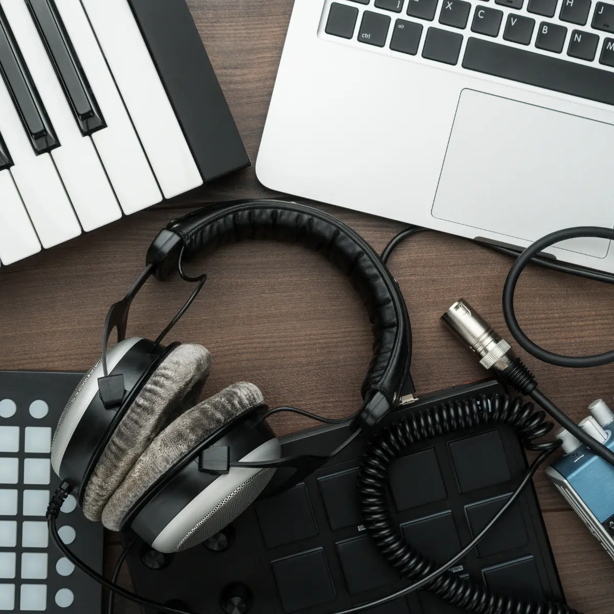 Music portfolio tools with headphones, MIDI controller, and laptop arranged on a wooden desk.