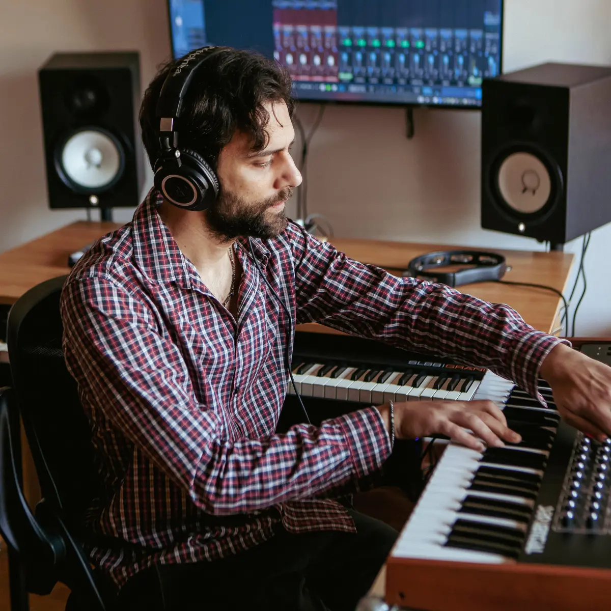 Music producer using MIDI keyboard and mixer in a home studio with headphones on.